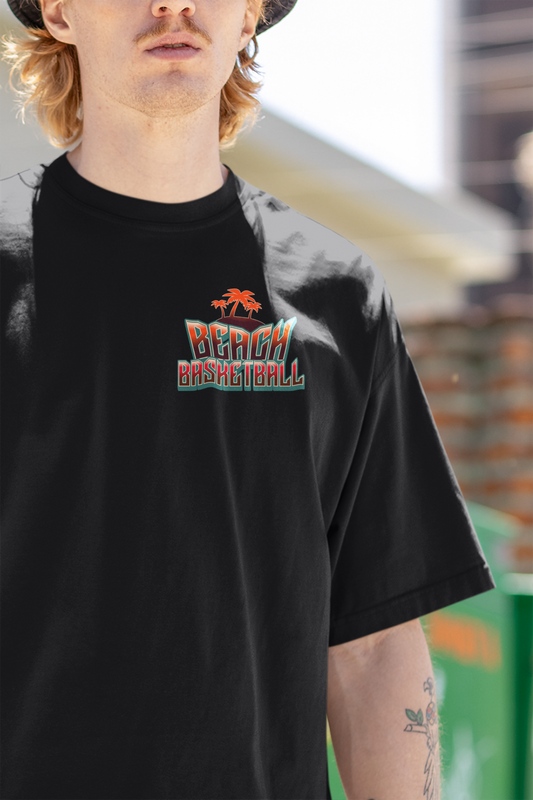 Kleiner "Beach Basketball" Retro-Print mit Palmen in Orange und Türkis auf der linken Brust eines Mockup mit Model auf einen schwarzen Oversized T-Shirts. 100% Baumwolle